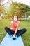 Vertical photo of a woman with mask facing the camera while stretching on the ground and doing a gesture to be fine with the