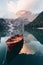 Vertical photo. Wooden boat on the crystal lake with majestic mountain behind. Reflection in the water