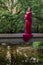 Vertical photo of young expecting mother wearing a red long dress standing on bridge