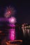 Vertical picture of colorful fireworks above the sea surrounded by buildings and lights in the night