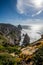 Vertical picture of rocks covered in greenery surrounded by the sea under the sunlight