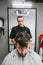 Vertical portrait of a barber cuts a bearded client in a men`s hairdresser, looking intently at the man`s hair. Male hairdresser