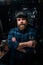 Vertical portrait of bearded cycling repairman in cap holding wrench standing by bicycle in repair workshop with dark