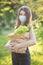 Vertical Portrait of Caucasian young pretty woman delivery worker in medical mask on the park carrying packet with fresh