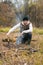 Vertical portrait of confident traveler male wearing warm clothes sitting near burning campfire and holding small shovel