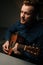 Vertical portrait of guitarist singer male playing acoustic guitar and singing song in dark living room at home studio.