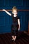 Vertical portrait of little blonde curly ballerina in black leotard practicing at ballet barre at dance studio. Kids hobby dancing