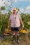 Vertical portrait of a senior farmer with two baskets full of fruits in the field after harvest