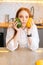 Vertical portrait of serious attractive redhead young woman holding in hands mango and avocado sitting at table with