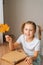 Vertical portrait of smiling little girl holding beautiful dried maple leaf to create herbarium diy at home.