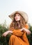 Vertical portrait of a young lady sitting in a field. Straw hat