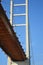 The vertical pylon and horizontal roadway of a bridge seen from below, against a blue sky