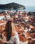 Vertical rear view shot of a girl standing on the city walls of Dubrovnik, looking towards the old red rooftops and the churches