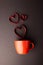 Vertical of red heart shapes rising from red mug on dark grey background, with copy space