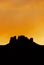 Vertical rock mesa silhouette under an orange sunset sky