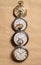 Vertical row of four antique gold and silver pocket watches on beige background. Retro mechanical watch with white dials