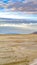 Vertical Sandy shore of a lake and distant rugged mountain under cloudy blue sky