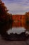 Vertical selective focus shot of a lake in the middle of brown and green trees under a cloudy sky