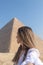Vertical selfie view of unrecognizable young blond woman taking a selfie sideways with the Pyramid of Cairo, Egypt in
