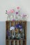 Vertical shot of assorted colorful flowers in individual vases on a two-layer wooden shelf