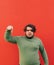 Vertical shot of an attractive emotional hispanic man standing on a red background, pointing his finger down, frowning, feeling