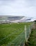 Vertical shot of barbed wire and chain link fence on a field with a view of a cliff on a seashore