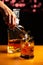Vertical shot of a bartender putting ice and splashing a glass of whiskey in a bar