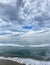 Vertical shot of a beautiful ocean with calm foamy waves under a blue cloudy sky