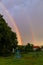 Vertical shot of the beautiful rainbow shining in the gloomy sky over the backyard with a swing