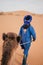 Vertical shot of a Berber walking through the Erg Chebli with a Camel
