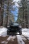 Vertical shot of a black Toyota Tacoma on the narrow trail between the snowy trees in a forest