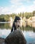 Vertical shot of black and white border collie stands on a large rock on the lake shore