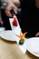 Vertical shot of a bokeh blurred male hand holding above a table a long kitchen knife with a small pile of red gari ginger and