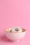 Vertical shot of a  bowl of powdered sugar donuts on pink background