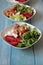 Vertical shot of bowls of salad with chicken, tomatoes, greens, and cheese