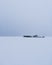 Vertical shot of buildings in the middle of a plain snow field under a very cloudy sky