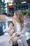 Vertical shot of businesswoman looking around, holding mobile phone, waiting at a meeting spot, sitting near fountain in