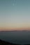 Vertical shot of a calm sea with the moon visible in the sky