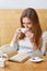 Vertical shot of carefree lovely woman drinks hot tea from white mug, reads fantastic story, likes book, poses in coffee shop,