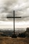 Vertical shot of a cross with an overlooking view of mountains under a cloudy gray sky