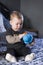 Vertical shot of cute fair baby girl sitting on bed examining duck toy