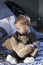 Vertical shot of cute fair baby girl sitting on bed looking at large vintage teddy bear