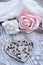 Vertical shot of decorated metallic heart next to white and pink roses on patterned white tablecloth