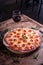 Vertical shot of a delicious cheesy pepperoni pizza with a glass of wine on a wooden table