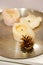 Vertical shot of a fir cone next to three white candles on a plate
