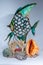 Vertical shot of a fish figurine with different seashells under it on a white surface and background