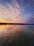 Vertical shot fluffy colorful clouds reflecting the sunset on the lake water surface. Calm, idyllic evening scene with lots of