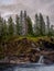 Vertical shot of a forested cliff by a river under a cloudy sky