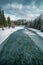 Vertical shot of a frozen turquoise river in an area covered with snow next to a forest