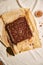 Vertical shot of a fudge brownie on a brown surface next to a bowl of walnuts and a large spoon